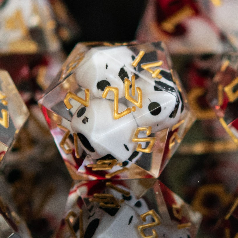 A set of clear sharp-edged resin dice with engraved numbers in gold, with white skulls and red blood inside including various shapes such as a d4, d6, d8, d10, d12, and d20 for tabletop and board games