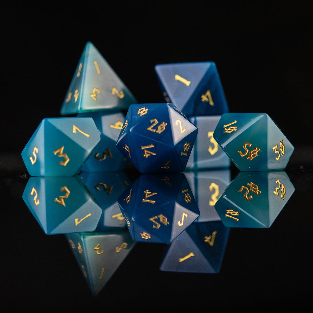 A set of blue agate stone dice with engraved numbers, displayed on a reflective surface.