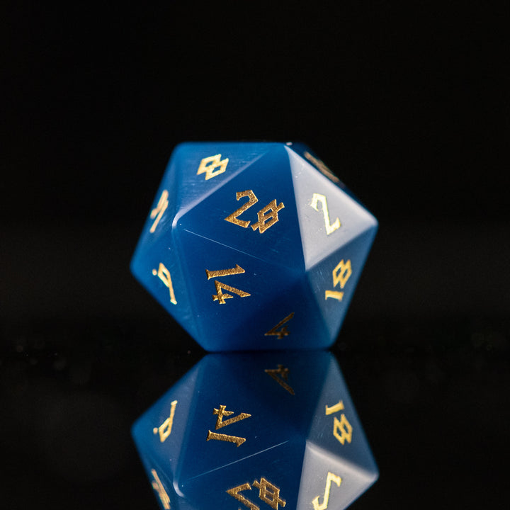 A set of blue agate stone dice with engraved numbers, displayed on a reflective surface.
