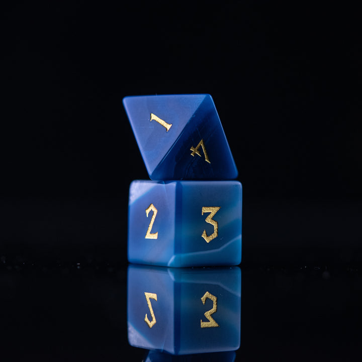 A set of blue agate stone dice with engraved numbers, displayed on a reflective surface.