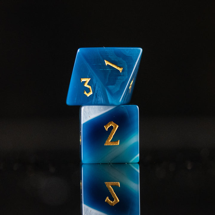 A set of blue agate stone dice with engraved numbers, displayed on a reflective surface.