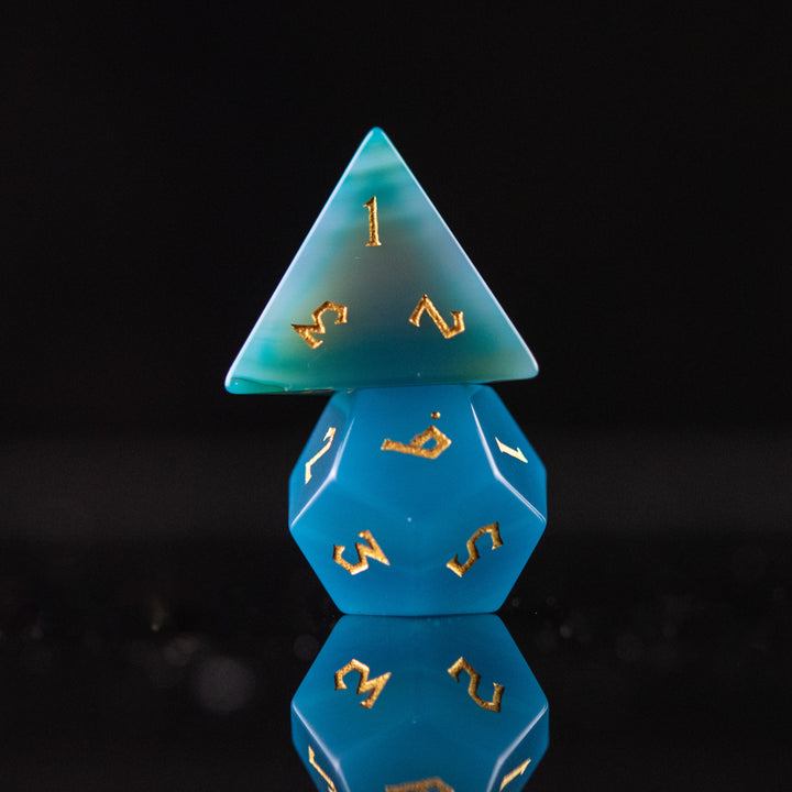 A set of blue agate stone dice with engraved numbers, displayed on a reflective surface.
