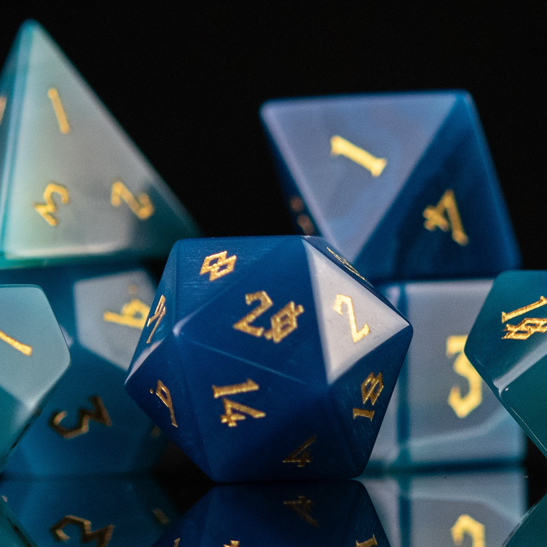 A set of blue agate stone dice with engraved numbers, displayed on a reflective surface.
