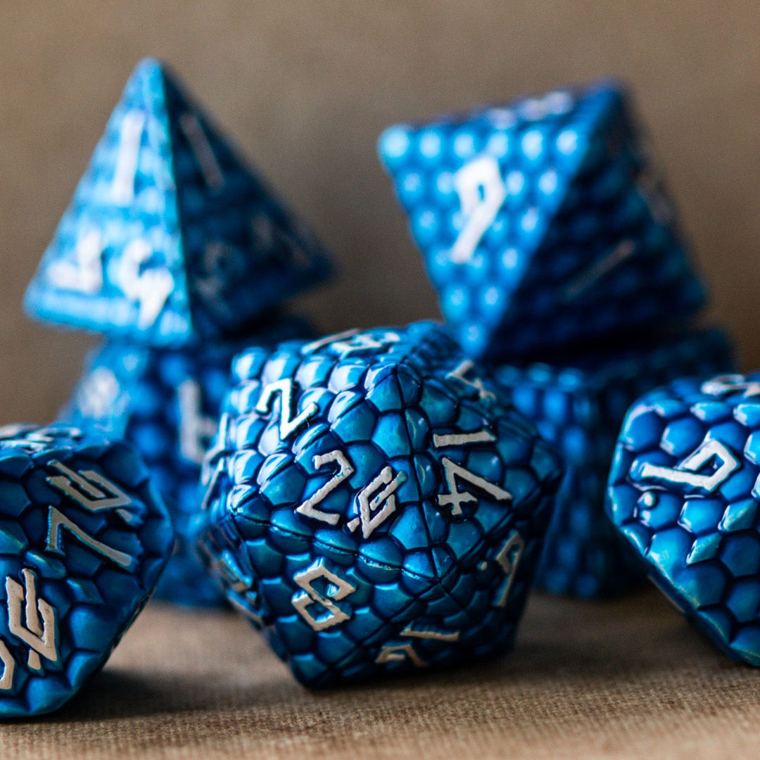 A set of blue dragon scale texture metal dice with embossed numbers, including various shapes such as a d4, d6, d8, d10, d12, and d20, displayed on a textured surface.