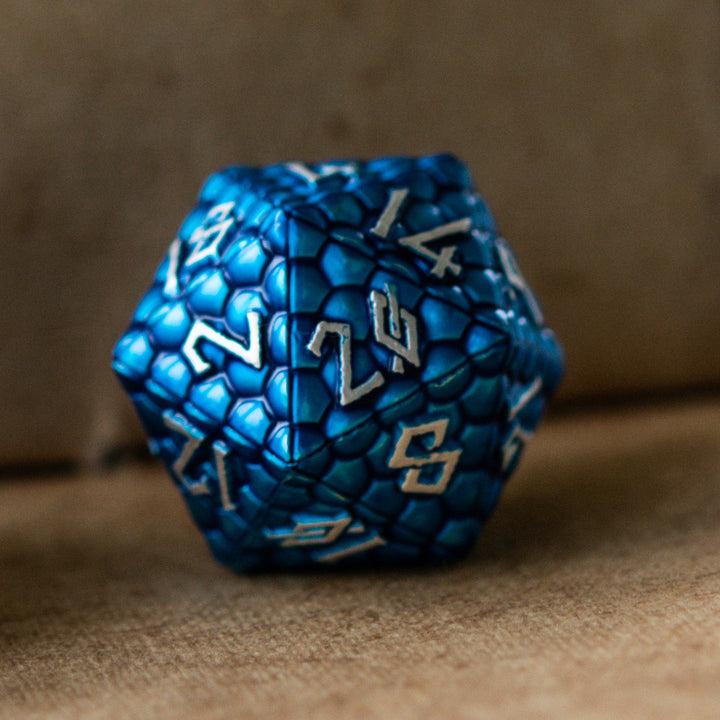 A set of blue dragon scale texture metal dice with embossed numbers, including various shapes such as a d4, d6, d8, d10, d12, and d20, displayed on a textured surface.