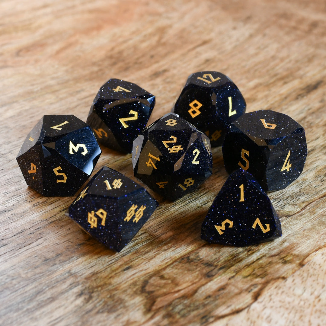 A set of black multifaceted stone dice with engraved numbers, displayed on a wooden surface.