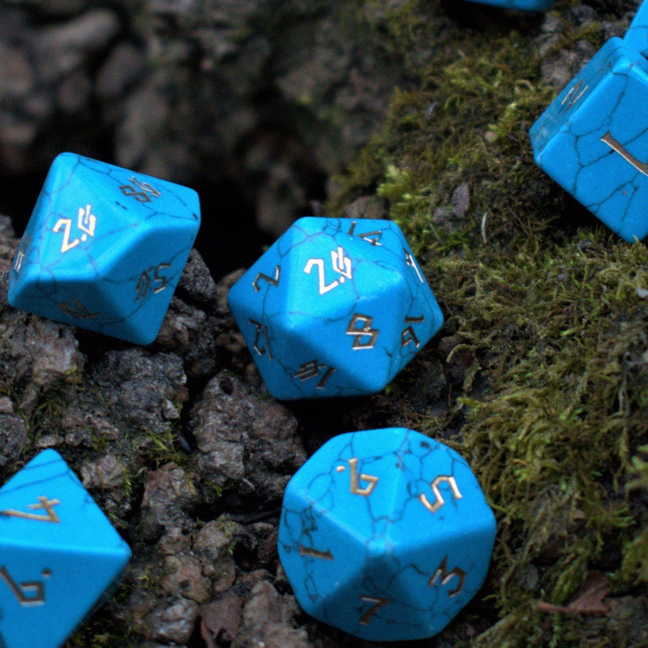 A set of blue turquoise stone dice with engraved numbers placed on a mossy surface.