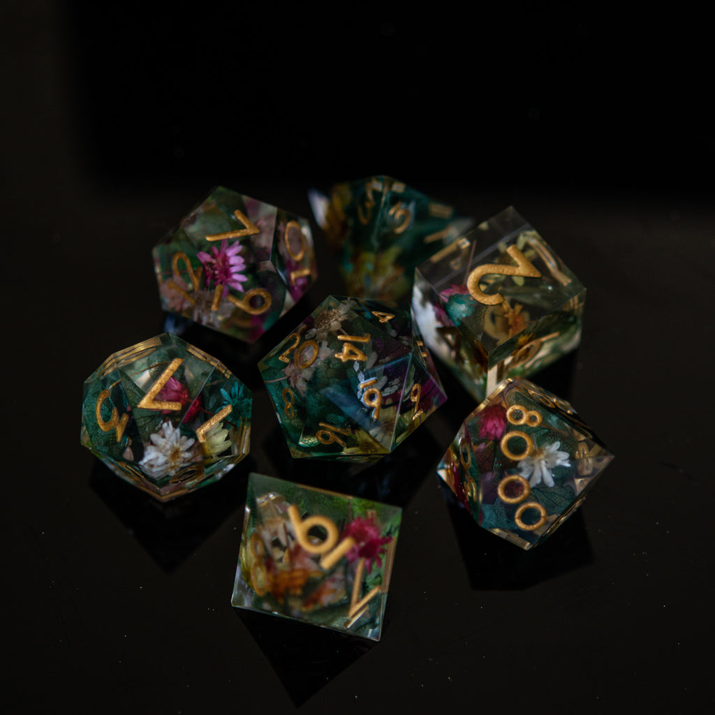 A set of sharp-edged, hand-painted resin dnd dice with floral and botanical designs, featuring gold, green, pink, and yellow colors for tabletop gaming and board games