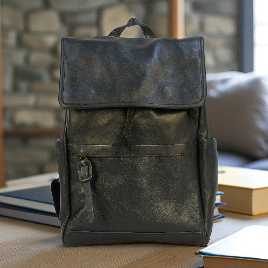 Dark leather navy modern rugged backpack on a wooden surface with books in the background