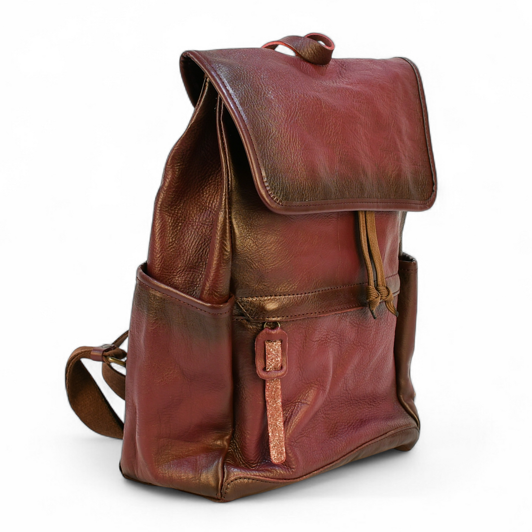 Purple modern rugged leather backpack on a rocky outcrop with a mountainous landscape and sunset in the background