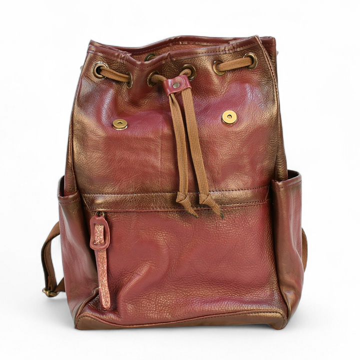 Purple modern rugged leather backpack on a rocky outcrop with a mountainous landscape and sunset in the background