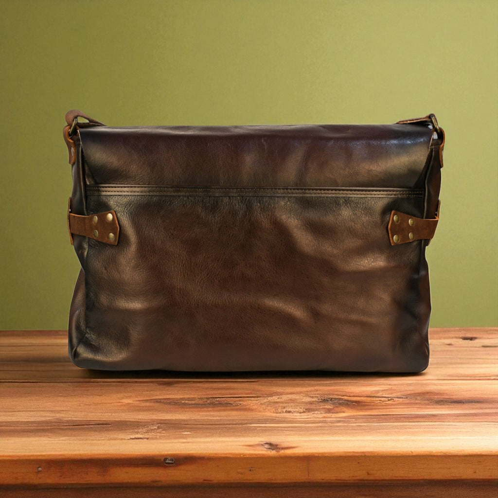Brown leather bag with gold accents on a wooden surface against a green wall