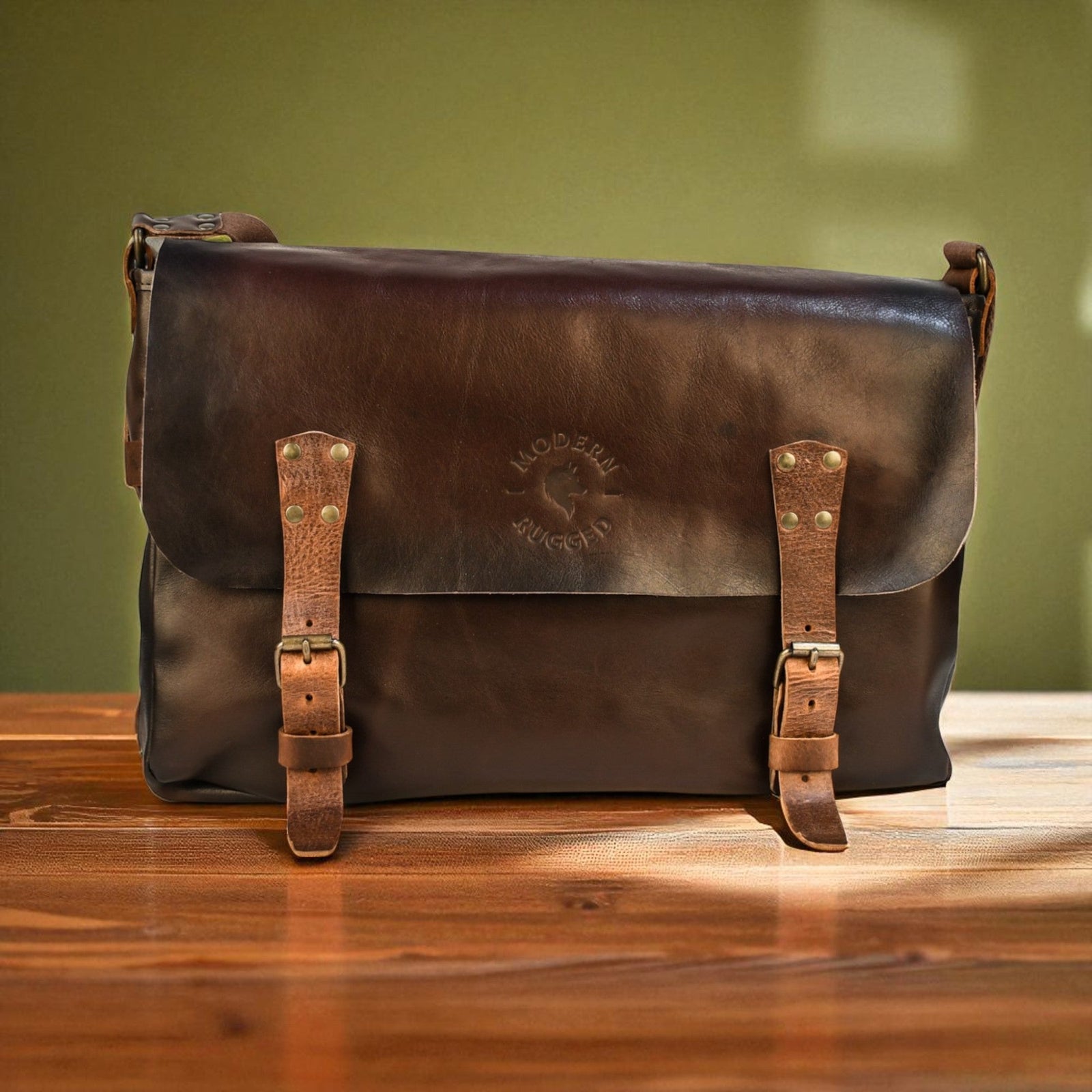Brown leather bag with straps on a wooden surface against a green wall