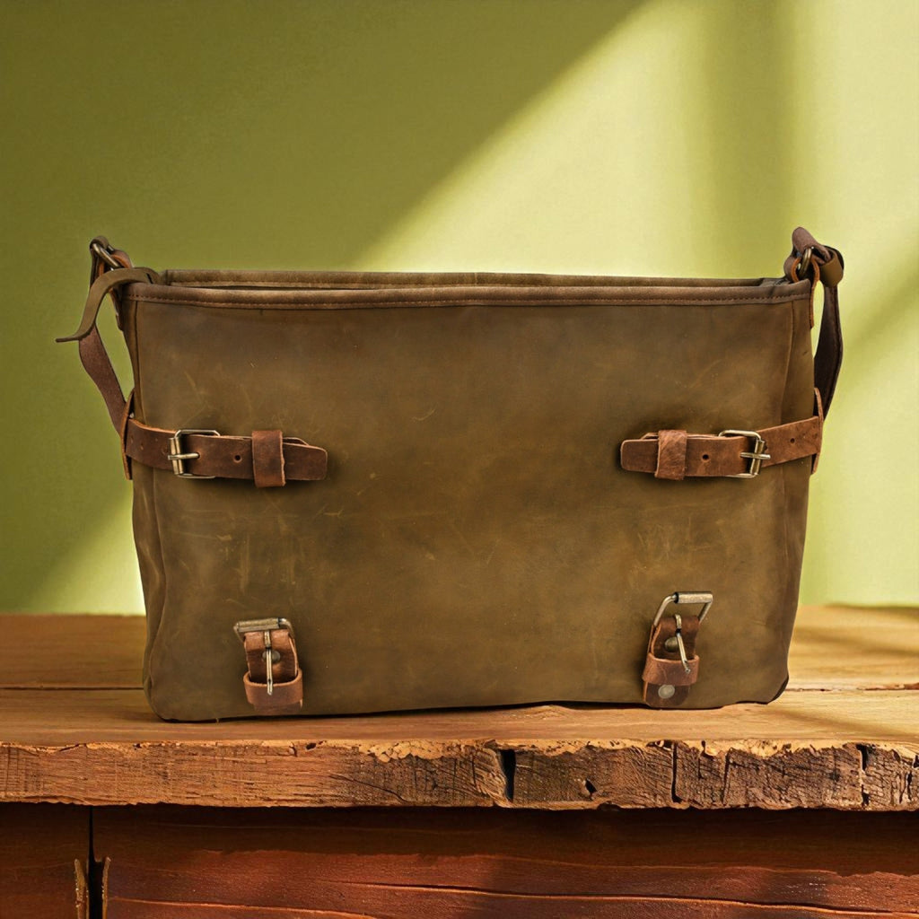 Brown leather bag with buckles on a wooden surface against a green background
