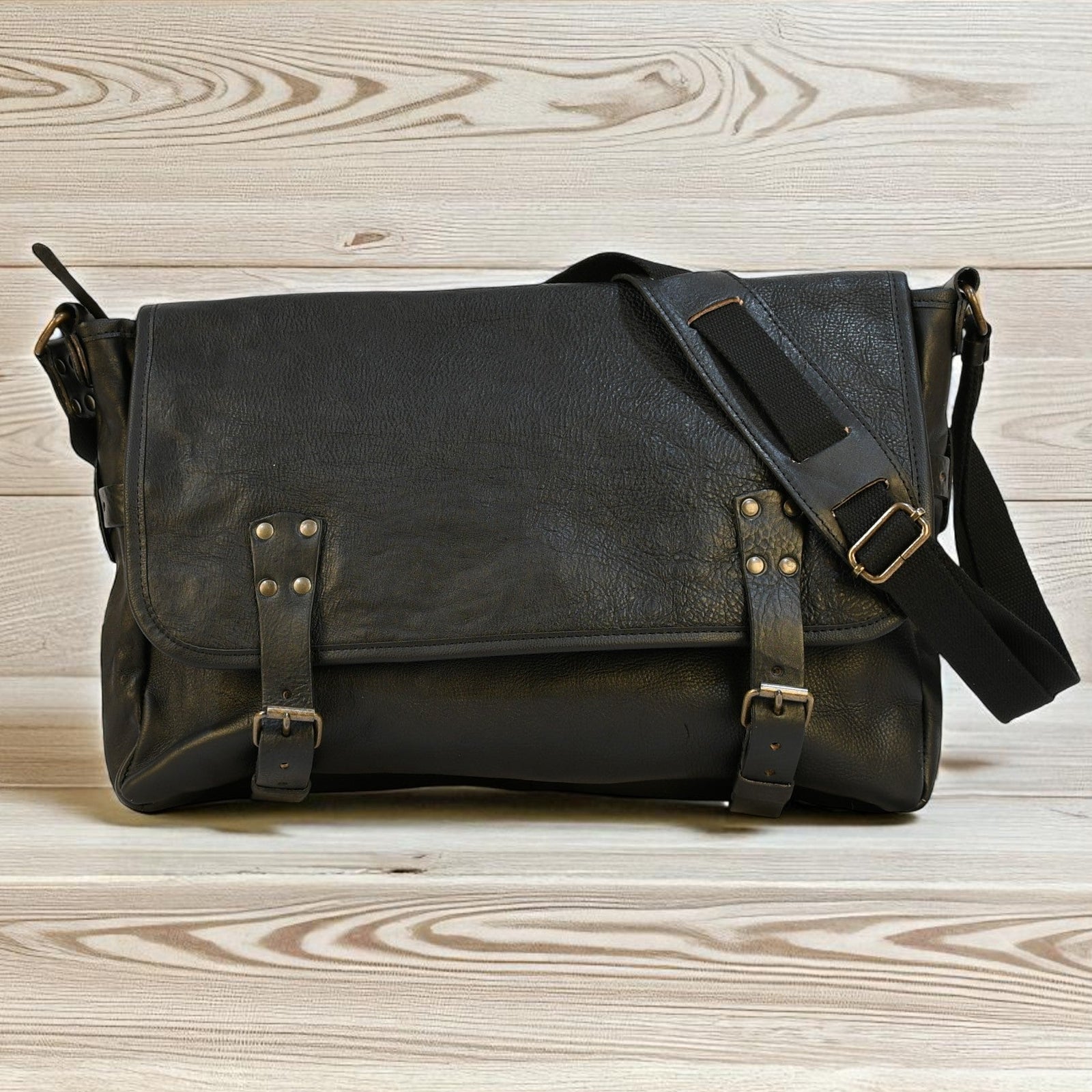 Black leather modern rugged messenger bag on a wooden surface