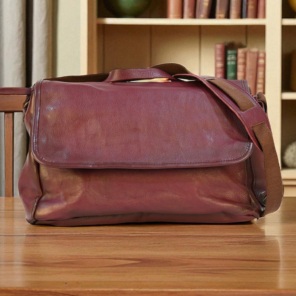 purple modern rugged leather messenger bag on a wooden table with a bookshelf in the background