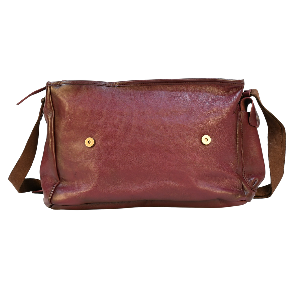 purple modern rugged leather messenger bag on a wooden table with a bookshelf in the background