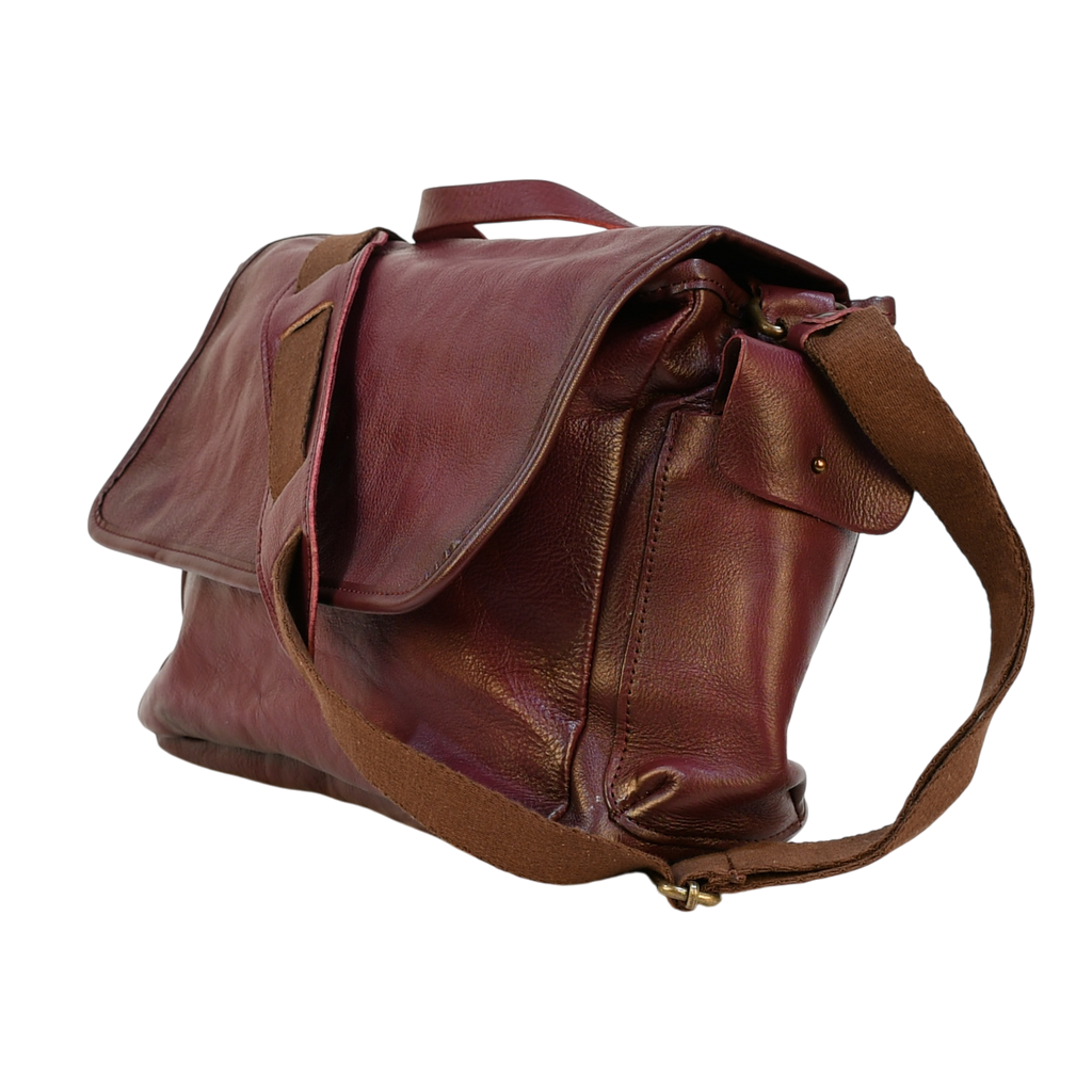 purple modern rugged leather messenger bag on a wooden table with a bookshelf in the background