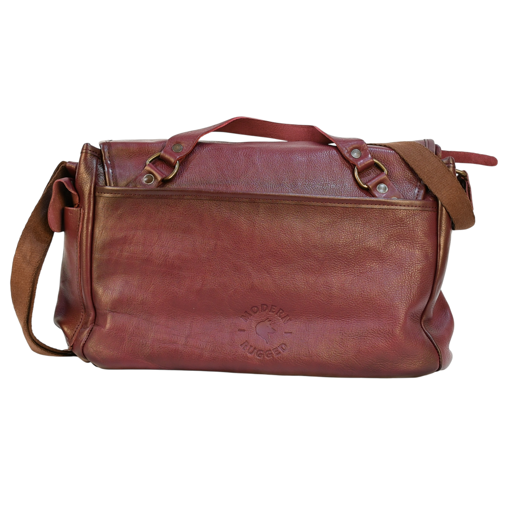 purple modern rugged leather messenger bag on a wooden table with a bookshelf in the background