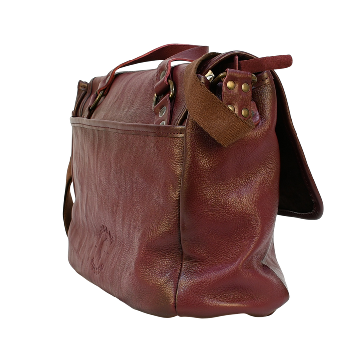 purple modern rugged leather messenger bag on a wooden table with a bookshelf in the background