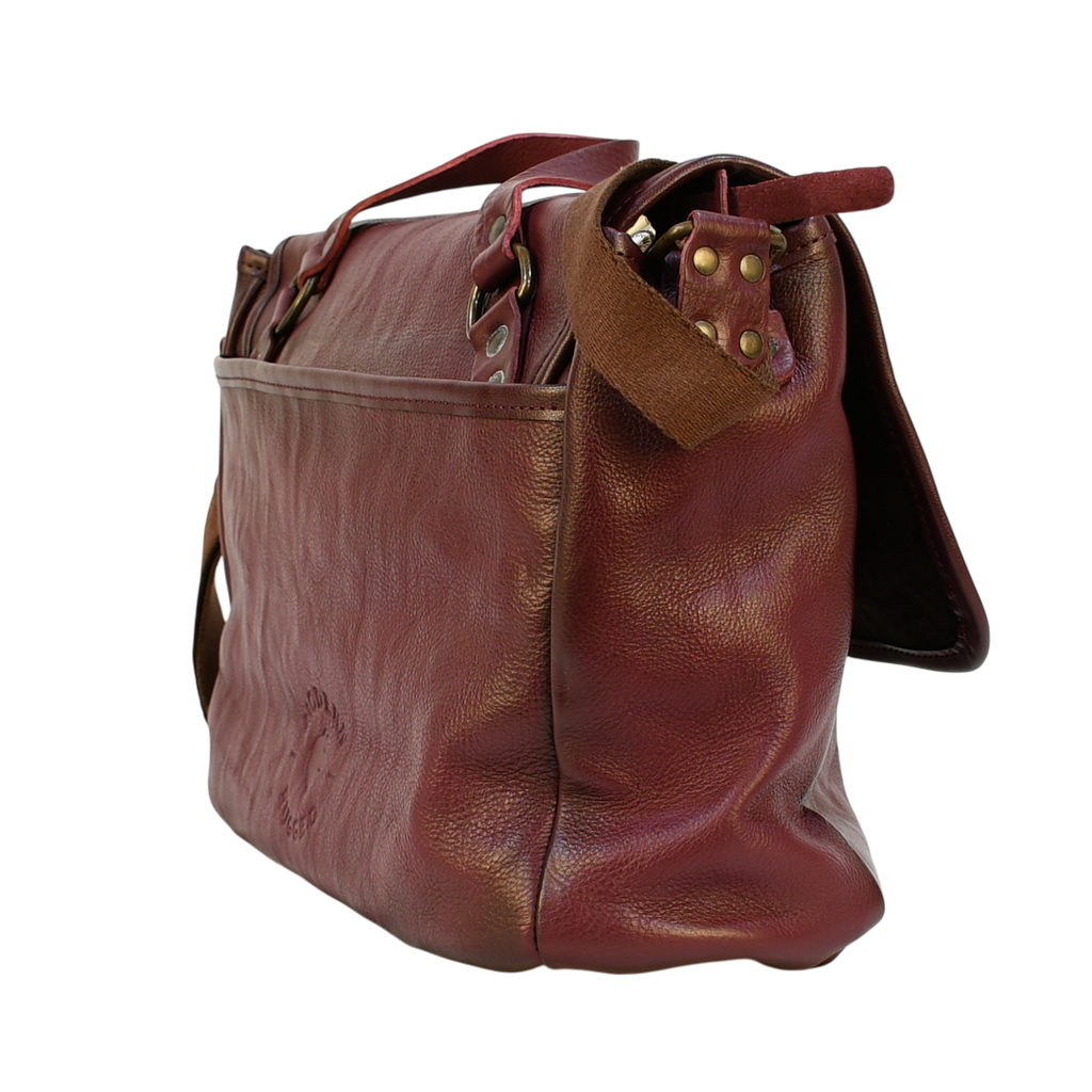 purple modern rugged leather messenger bag on a wooden table with a bookshelf in the background