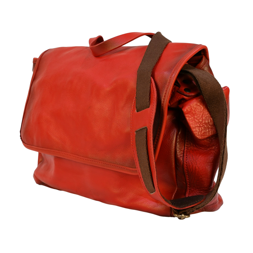 Red leather modern rugged messenger bag on a wooden surface with books in the background