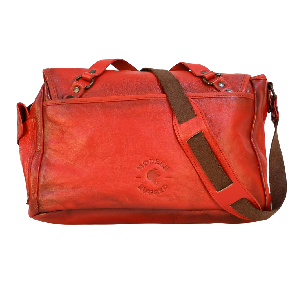 Red leather modern rugged messenger bag on a wooden surface with books in the background