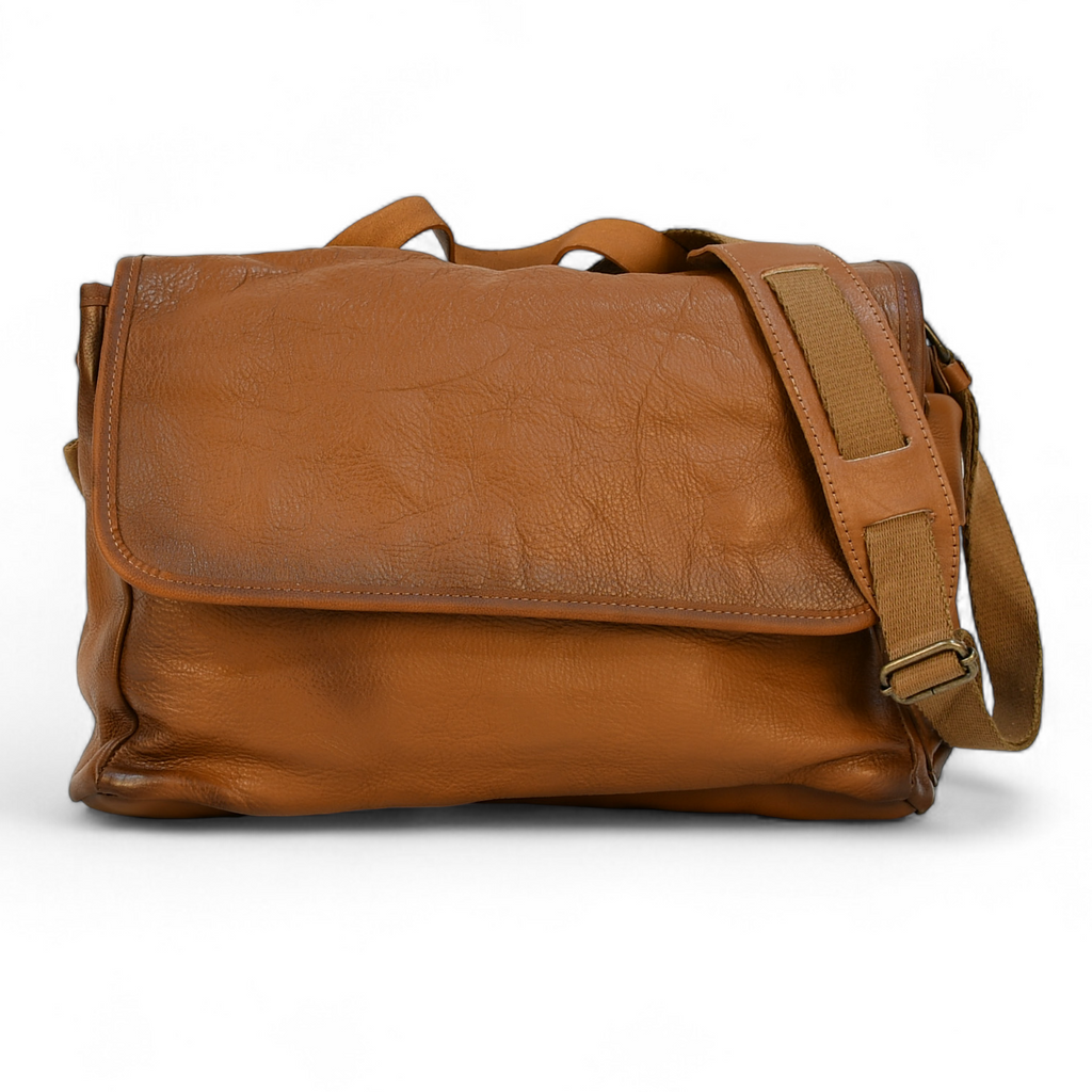 Brown leather modern rugged messenger bag on a surface with a window in the background