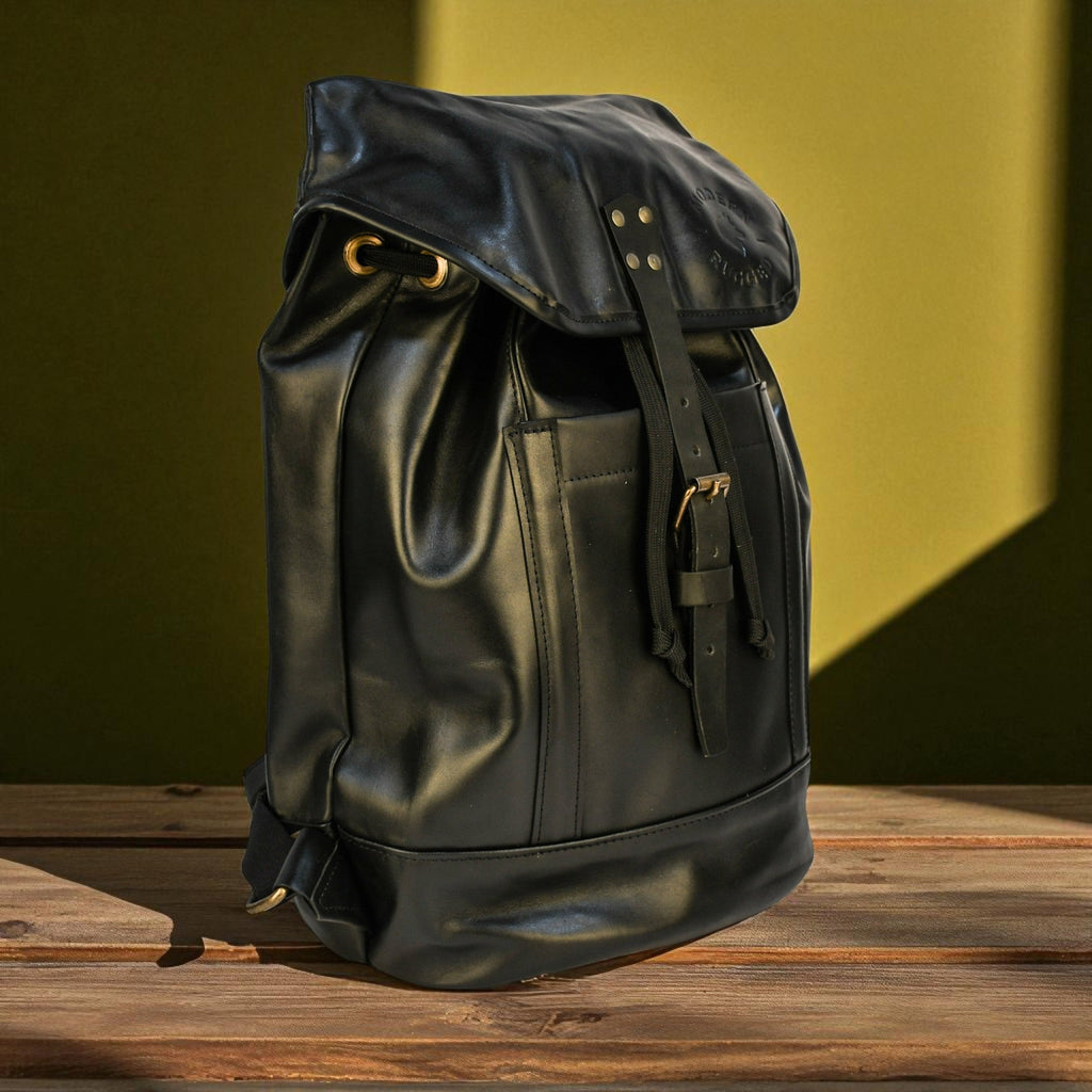 Black leather backpack on a wooden surface with a green background