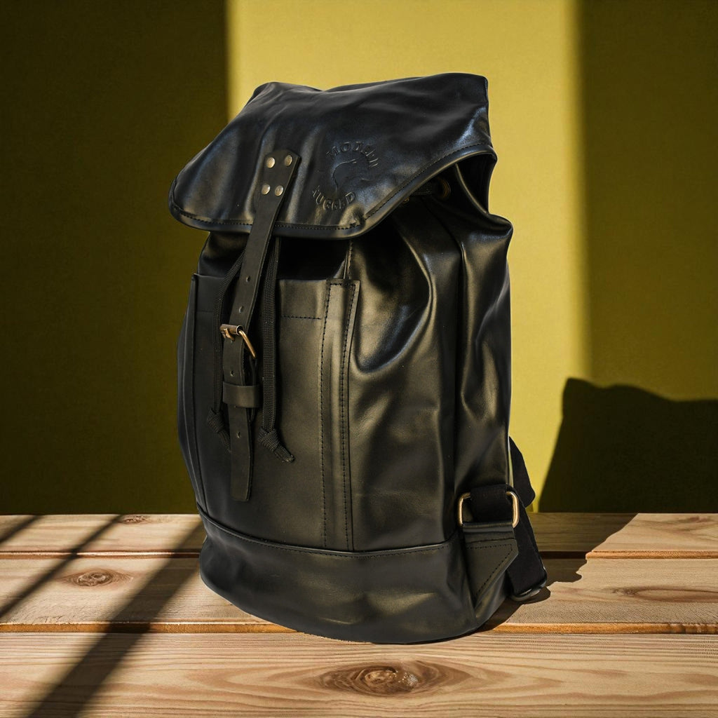 Black leather backpack on a wooden surface with a green wall background