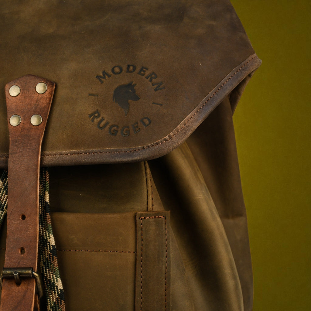 Brown leather backpack with 'Modern Rugged' logo on a green background