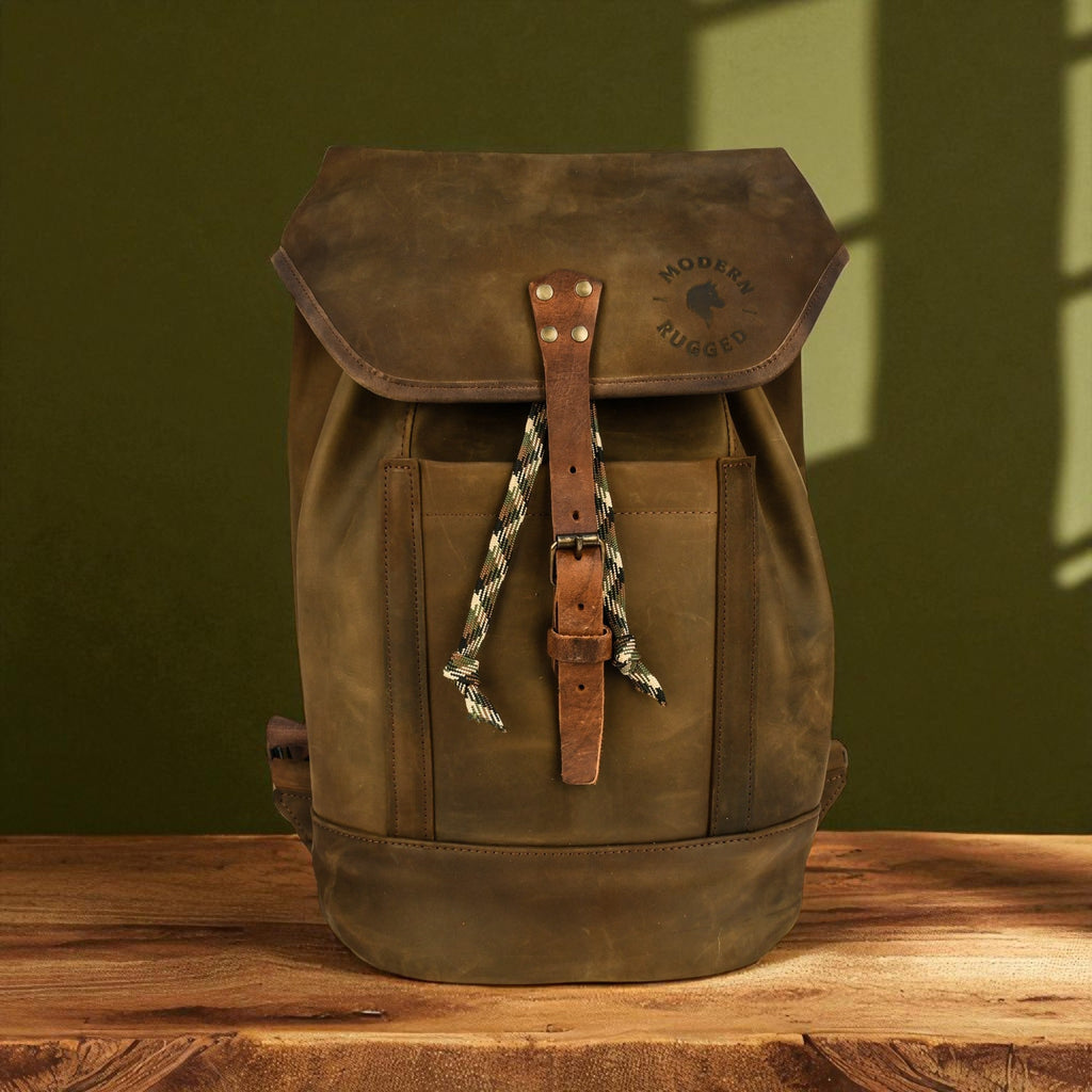 Brown leather backpack with a strap on a wooden surface against a green wall