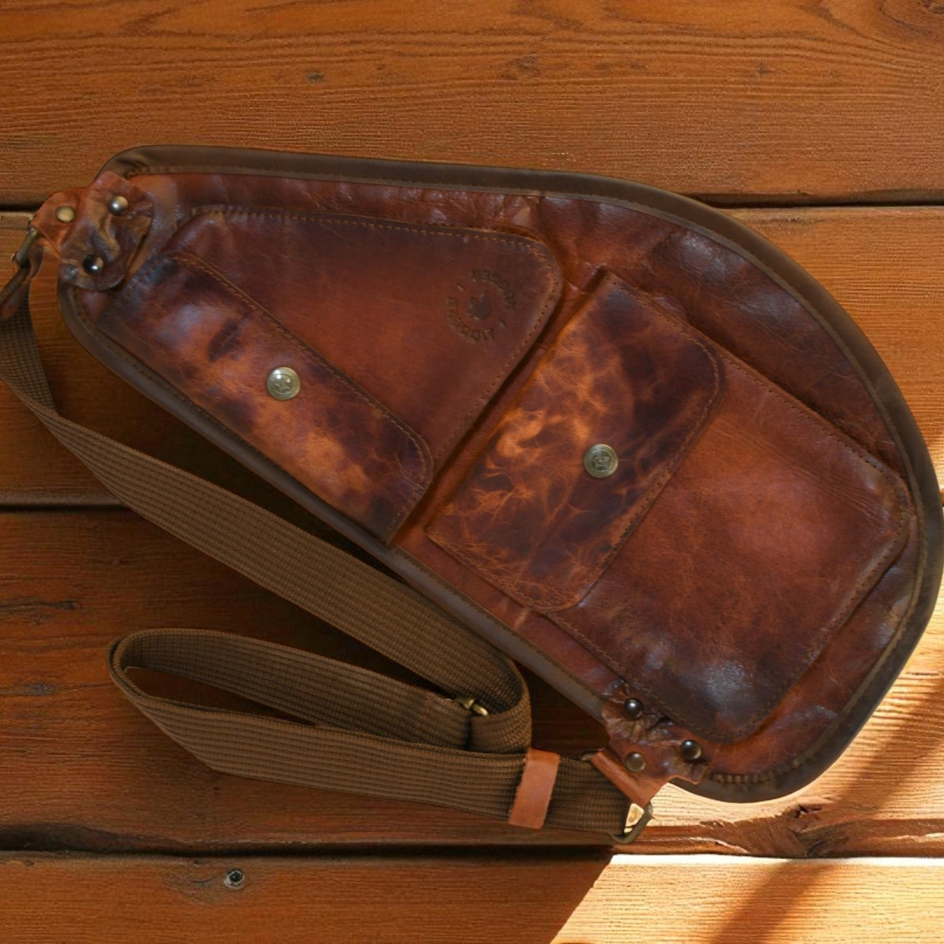 Brown leather bag with a strap on a wooden surface