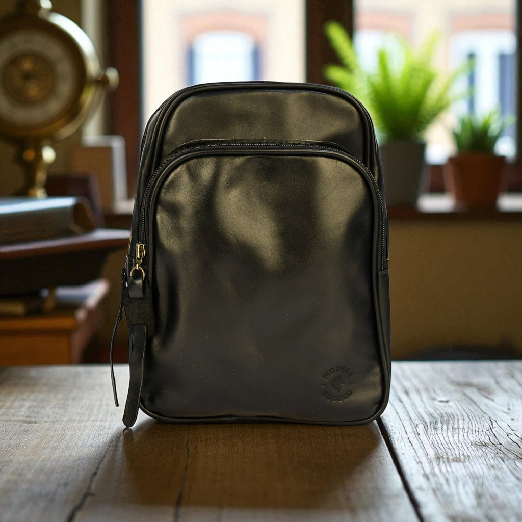 Black bovine leather sling bag on a wooden table with a blurred indoor background