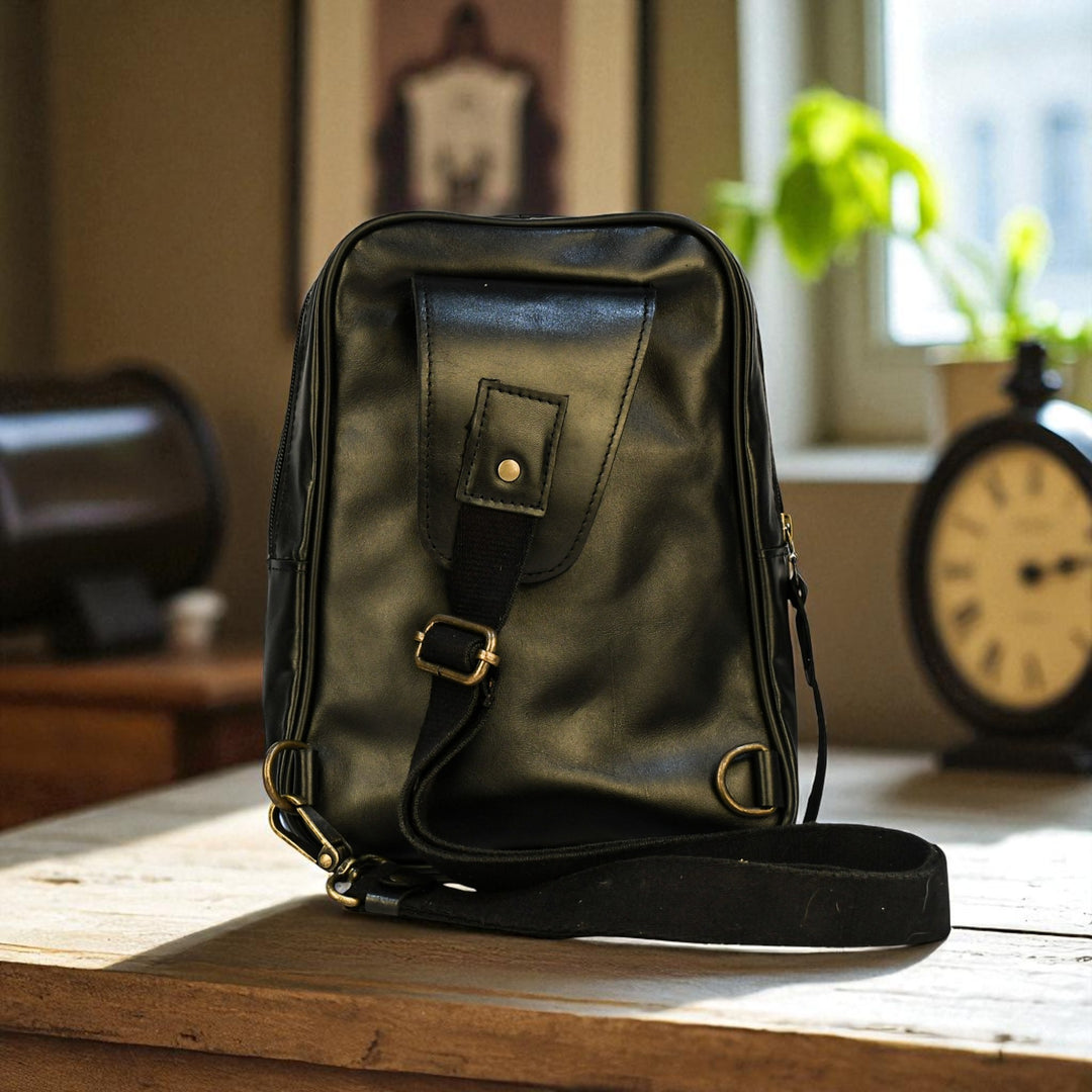 Black bovine leather sling bag on a wooden table with a blurred indoor background