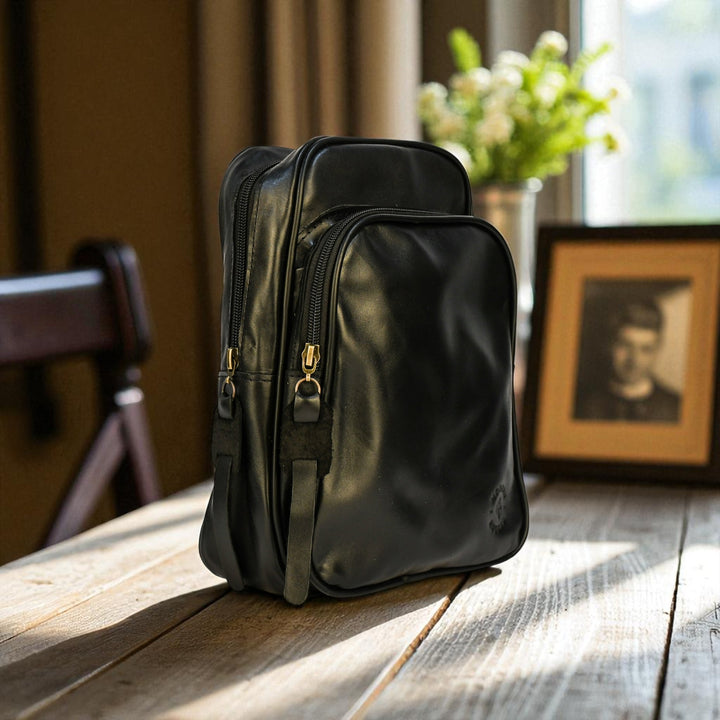 Black bovine leather sling bag on a wooden table with a blurred indoor background