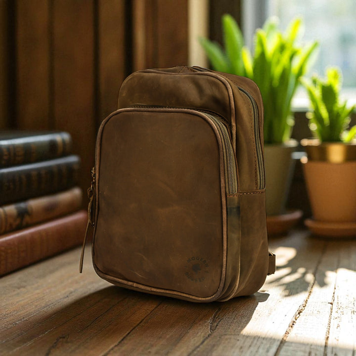 olive leather sling bag on a wooden surface with books and plants in the background