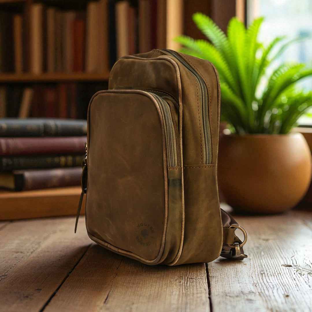 olive leather sling bag on a wooden surface with books and plants in the background