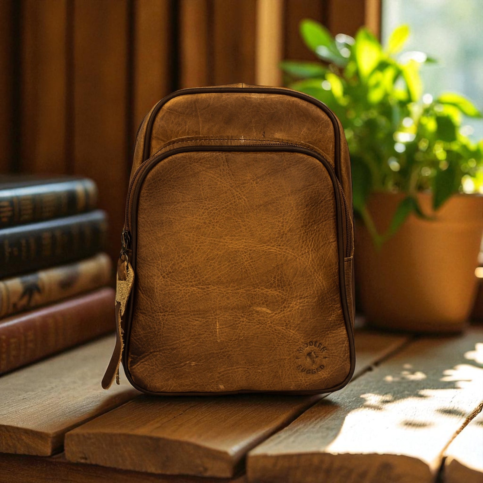 Brown leather backpack on a wooden surface with books and a plant in the background