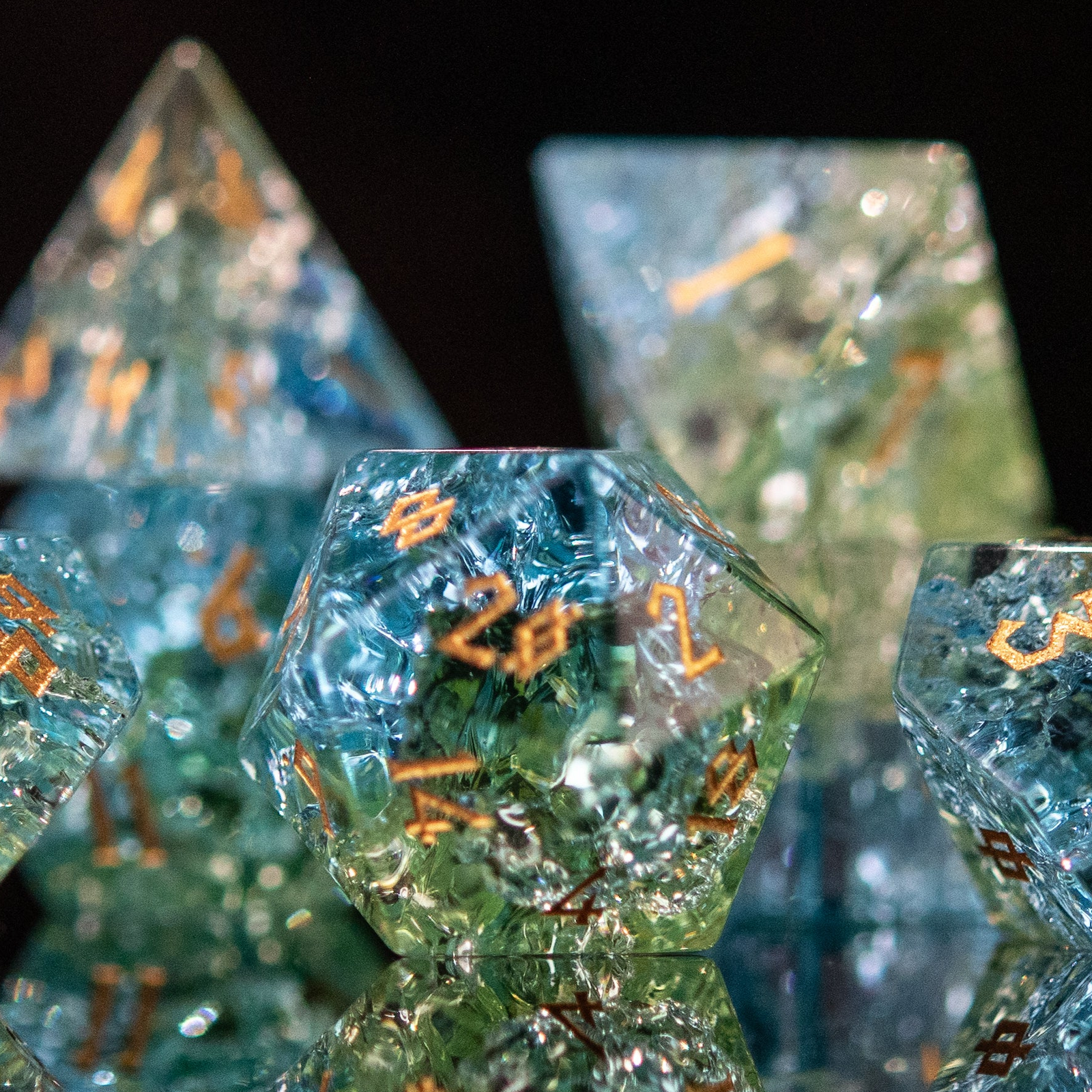 A set of hand-carved, shattered glass dnd dice with engraved and gold painted numbers, featuring shades of blue and green.