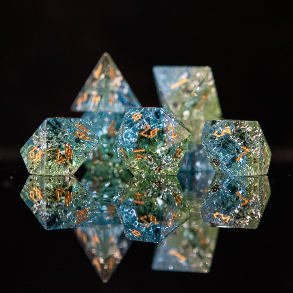 A set of hand-carved, shattered glass dnd dice with engraved and gold painted numbers, featuring shades of blue and green.