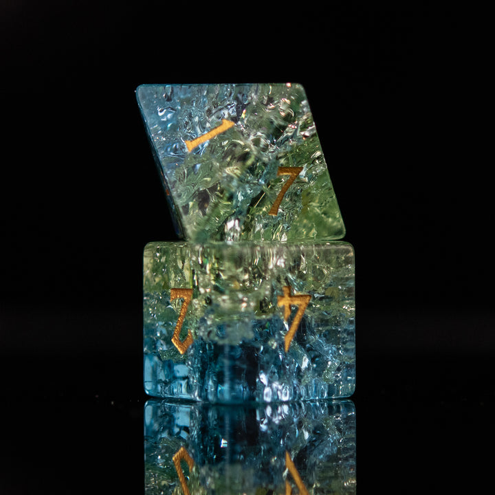 A set of hand-carved, shattered glass dnd dice with engraved and gold painted numbers, featuring shades of blue and green.