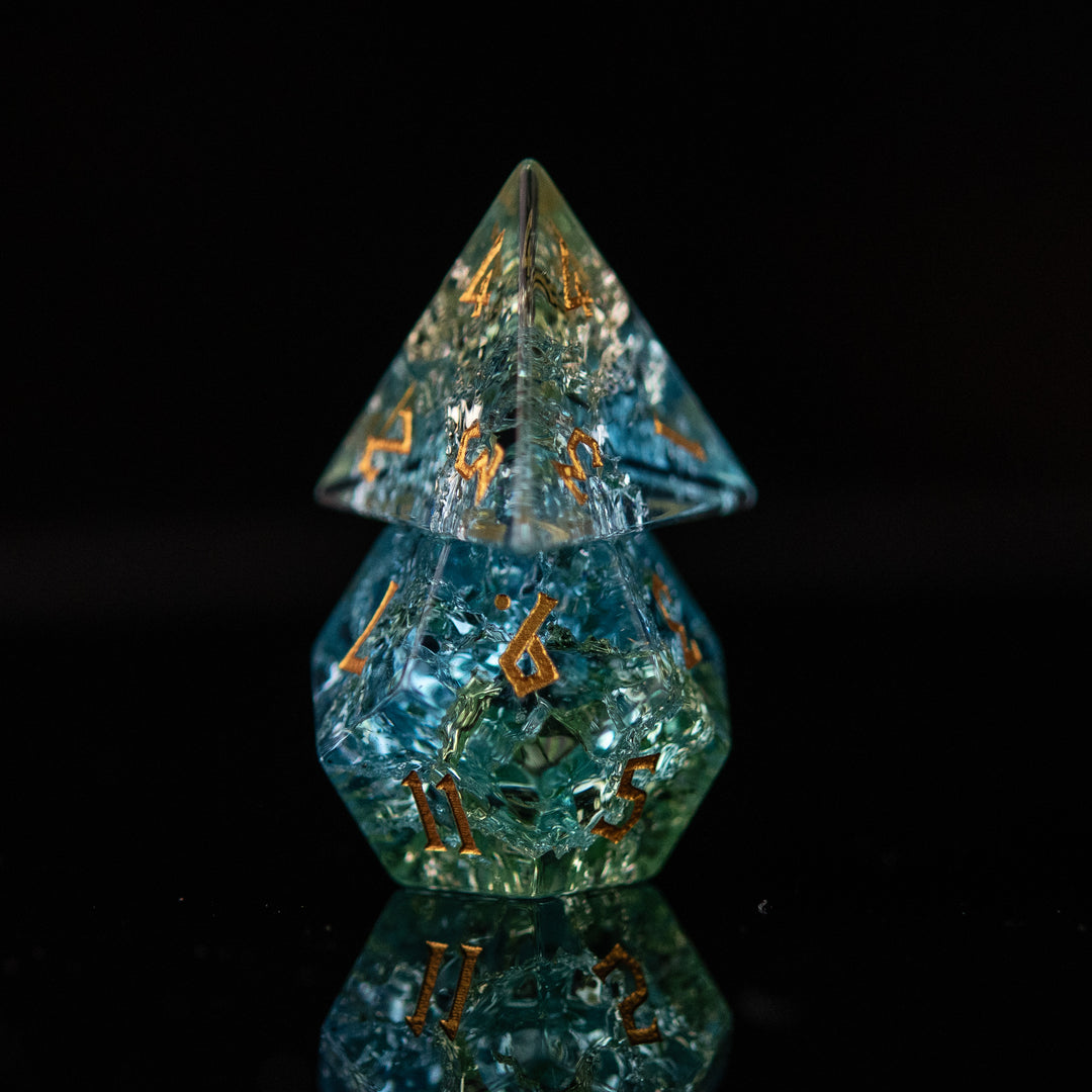 A set of hand-carved, shattered glass dnd dice with engraved and gold painted numbers, featuring shades of blue and green.