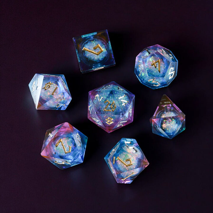A set of resin dice with a liquid core, featuring a celestial galaxy pattern, laid out on a dark background.