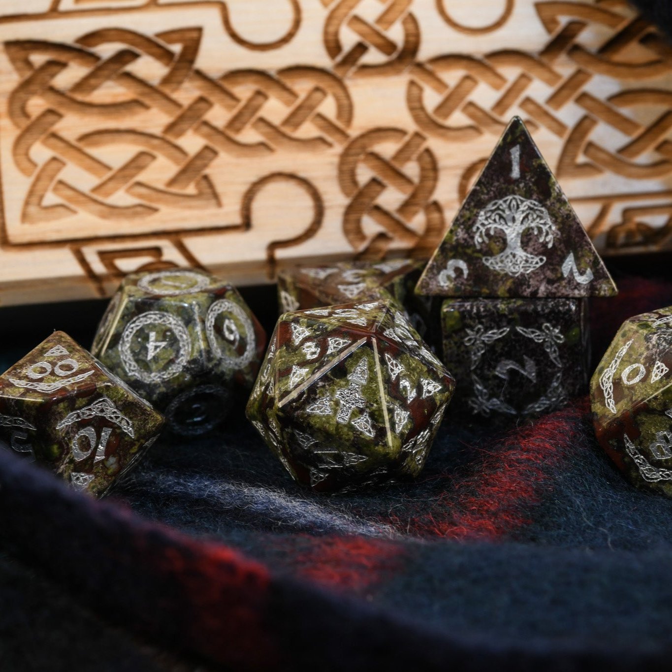A set of hand-carved Celtic Dragon Blood Jasper Stone Dice with engraved numbers, displayed on a tartan surface with Celtic knot patterns.