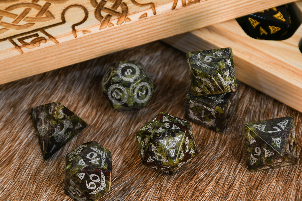 A set of hand-carved Celtic Dragon Blood Jasper Stone Dice with engraved numbers near a dnd dice vault engraved with celtic knots