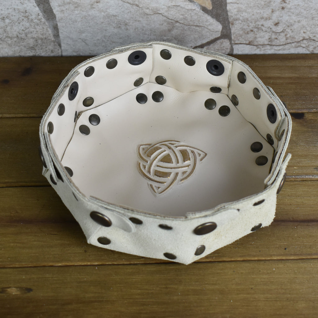 An octagonal Celtic knot leather dice tray with snap buttons and a gold-colored knot design in the center, displayed on a wooden surface.
