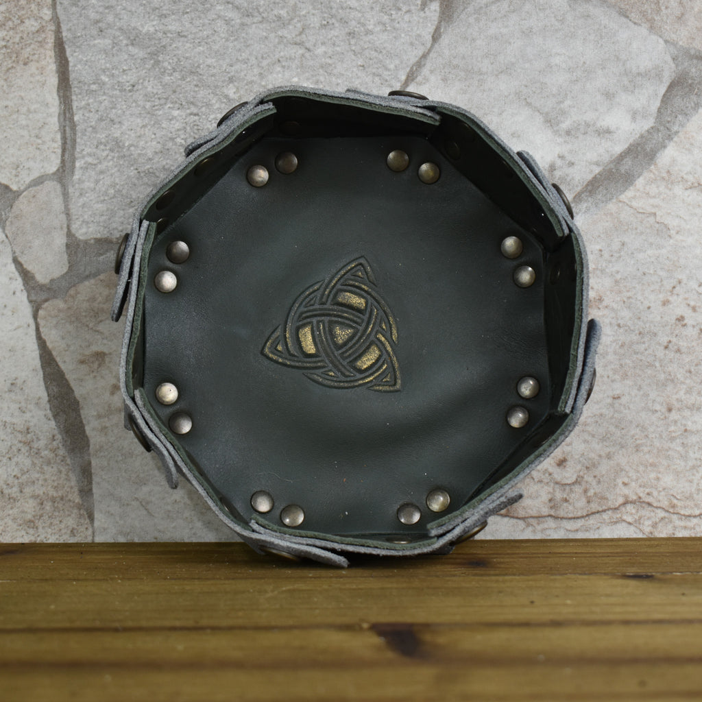 An octagonal Celtic knot leather dice tray with snap buttons and a gold-colored knot design in the center, displayed on a wooden surface.