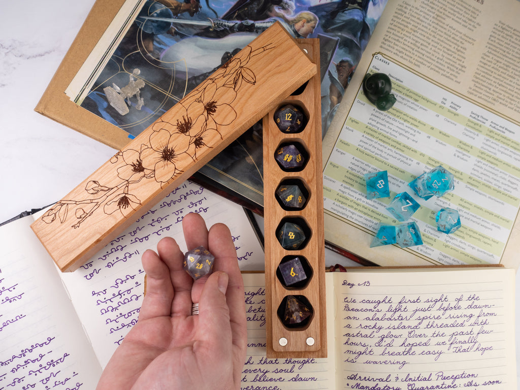 Wooden dice holder with six-sided dice, held by a hand, on top of a book with game rules.