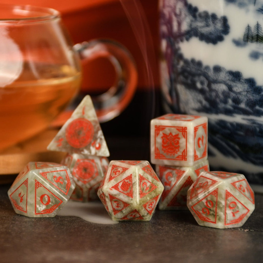 A set of hand-carved, Chinese Jade Stone Dice traditional Chinese patterns, displayed on a table with a cup and saucer in the background.